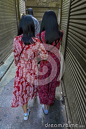 Moslem People of Egypt go shopping at Luxor Souq - two women wear bright red dresses from behind Editorial Stock Photo