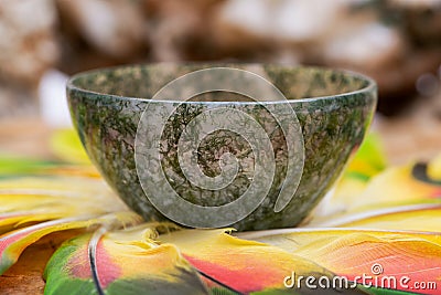 Moss Agate hand carved polished bowl in the middle of a circle made of colorful parrot feathers. Stock Photo