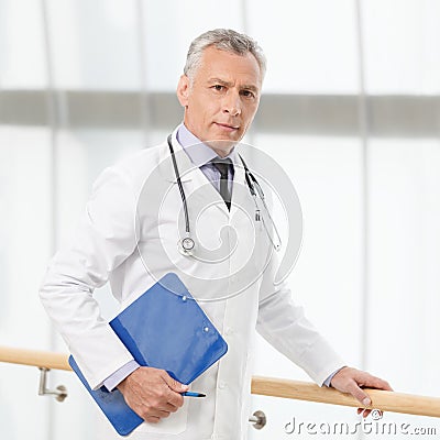 The most talented and professional doctor. Confident mature doctor standing with a clipboard and looking at camera Stock Photo