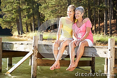 Mother and adult daughter sitting by lake Stock Photo