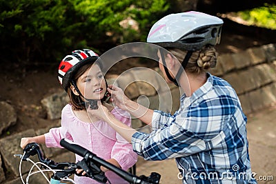 Mother assisting daughter in wearing bicycle helmet in park Stock Photo