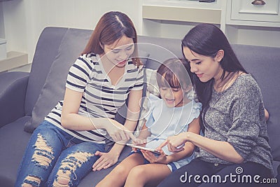 Mother, Aunt and kid having time together lerning with using tablet at home with relax and happy on couch Stock Photo