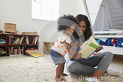 Mother And Baby Daughter Reading Book In Playroom Together Stock Photo