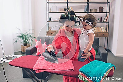 Mother and baby together engaged in housework Ironing clothes . Housewife and kid doing homework. Woman with little Stock Photo