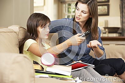 Mother Becoming Frustrated As Daughter Watches TV Whilst Doing Homework Sitting On Sofa At Home Stock Photo