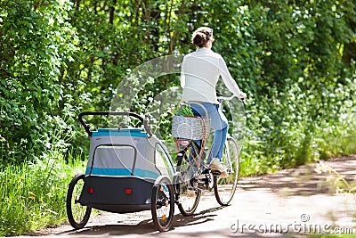 Mother on bicycle with baby bike trailer in park Stock Photo