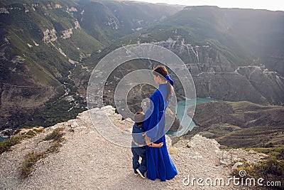 mother in a blue dress with her son stands on the cliff of the Sulak canyon Stock Photo