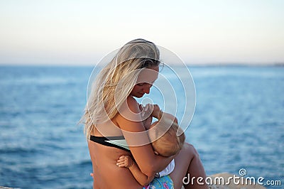 Mother breastfeeding baby on the beach at sunset near the sea. Positive human emotions, feelings, joy. Funny cute child making vac Stock Photo