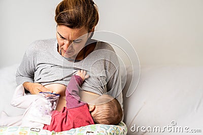 Mother breastfeeding her newborn baby while pumping milk from her other breast to store it in a special breastfeeding bag Stock Photo