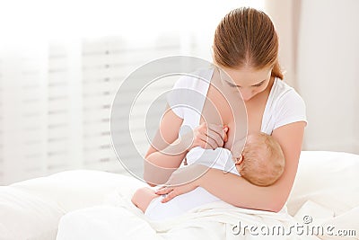 Mother breastfeeding newborn baby in white bed