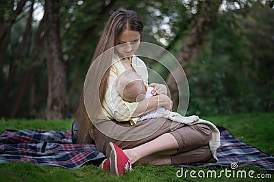 Mother breastfeeds her baby. Mom with a newborn sitting on picnic blanket Stock Photo