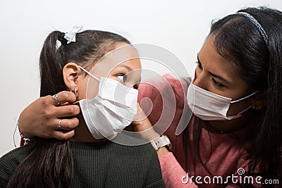 Mother cares for and puts the medical mask on her daughter to prevent illness. Woman wears a smart watch. Little girl looks to her Stock Photo