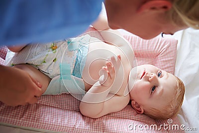 Mother Changing Baby Son's Nappy As He Lies On Mat Stock Photo