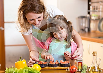 Mother with child daughter preparing fish in Stock Photo