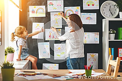 Mother and child girl hang their drawings on wall Stock Photo