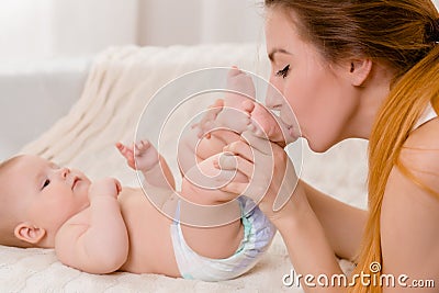 Mother and child on a white bed. Mom and baby girl in diaper playing in sunny bedroom. Stock Photo