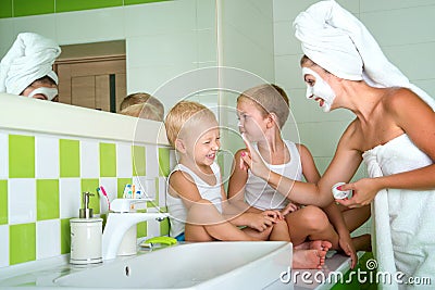 Mother and children make a face mask in the morning. The boys joke with mom. Stock Photo