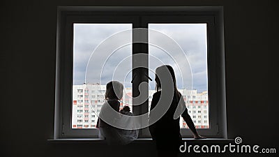 Mother comes to her lonely daughter who is sitting by the window. Stock Photo