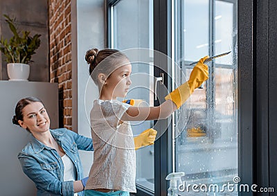 Mother and cute little daughter in protective gloves cleaning window together Stock Photo