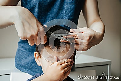 Mother cutting child`s hair at home. Child is afraid to get a haircut. Barber home. Haircut at home Stock Photo