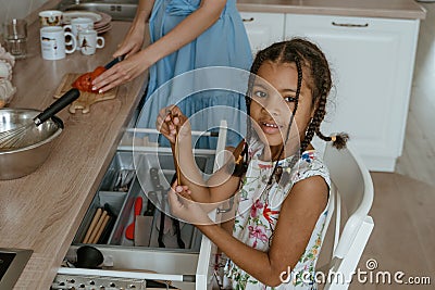 Mother is cutting the vegetable whit the young girl is playing with thread with an open knife shelf. Stock Photo