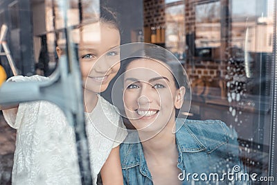 Mother and daughter cleaning window and smiling at camera Stock Photo