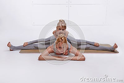 Mother daughter doing yoga exercise, fitness family sports, sports paired woman sitting on the floor stretching his legs apart in Stock Photo