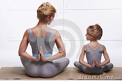 Mother and daughter doing yoga exercise, fitness, gym wearing the same comfortable tracksuits, family sports, sports paired siting Stock Photo