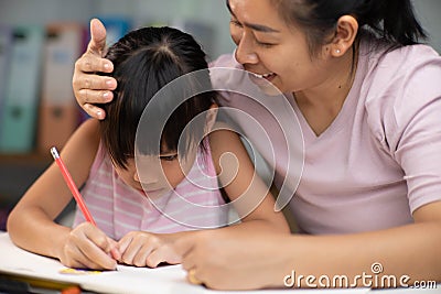 Mother and daughter drawing together with crayons. Adult woman helps girl study or draw together at home in living room. Happy Stock Photo