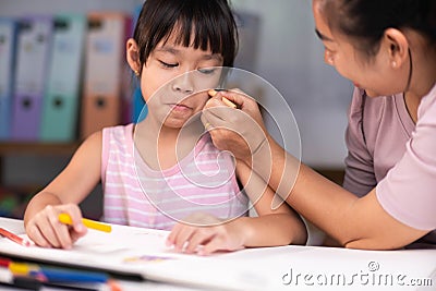 Mother and daughter drawing together with crayons. Adult woman helps girl study or draw together at home in living room. Happy Stock Photo