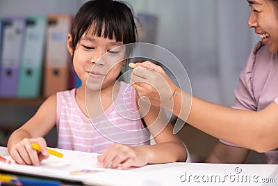 Mother and daughter drawing together with crayons. Adult woman helps girl study or draw together at home in living room. Happy Stock Photo