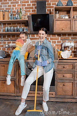 Mother and daughter with duster and broom having fun while cleaning home Stock Photo