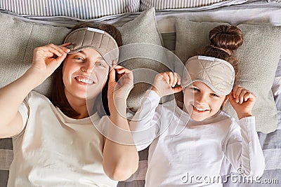 Mother and daughter enjoyed lazy morning together in cozy bedroom, wake up slowly, taking off blindfolds looking at camera smiling Stock Photo