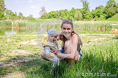 Mother and daughter happy family in a meadow on the shore of the lake in the grass Stock Photo