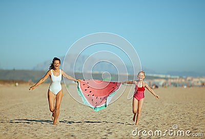 Mother and daughter holding funny watermelon towel and running Stock Photo