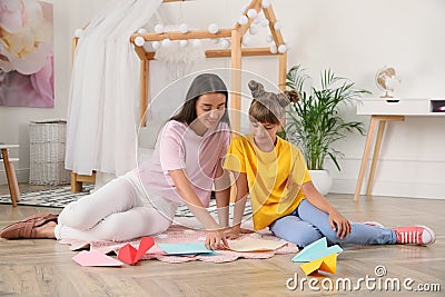 Happy mother and daughter making paper planes on floor in room Stock Photo