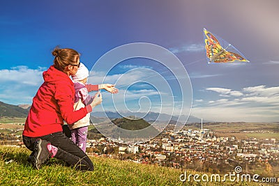 Mother and daughter playfull with kite in field over town Stock Photo