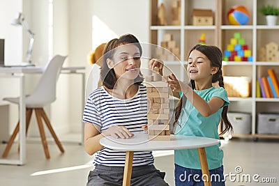 Mom and daughter playing and building tower out of wood blocks in cozy nursery at home Stock Photo