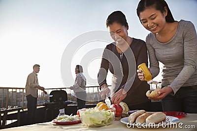 Mother and daughter preparing hot dogs for barbeque, father and son preparing sausages on barbeque Stock Photo