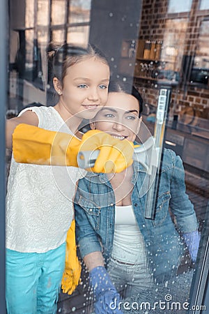 Mother and daughter in protective gloves cleaning window together Stock Photo