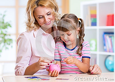 Mother and daughter putting coins into piggy bank Stock Photo