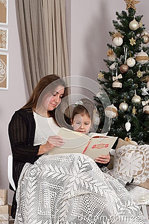 Mother and daughter read a book at fireplace on Christmas eve. Stock Photo