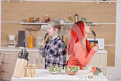 Mother and daughter singing on kitchen intruments Stock Photo