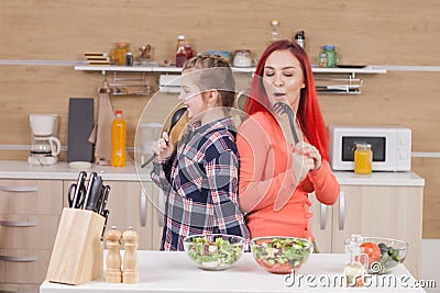 Mother and daughter singing on kitchen intruments Stock Photo