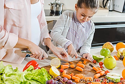 partial view of mother with daughter slicing carrots on chopping board Stock Photo