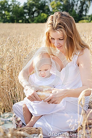 Mother and daughter in wheat field. Happy Family outdoors. healthy child with mother on picnic with bread and milk in golden Stock Photo