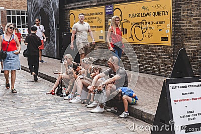 Mother, father, daughter and three sons sitting on the side of a road in Brick Lane Market in London Editorial Stock Photo