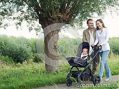 Mother and father walking outdoors and pushing baby in pram Stock Photo