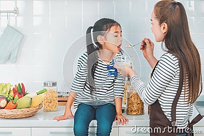 Mother feeding child with cereal on kitchen counter for breakfast with vegetable and ingredient on background Stock Photo