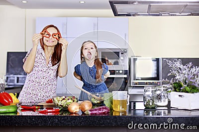 Mother and funny daughter playing in the kitchen with vegetables Stock Photo